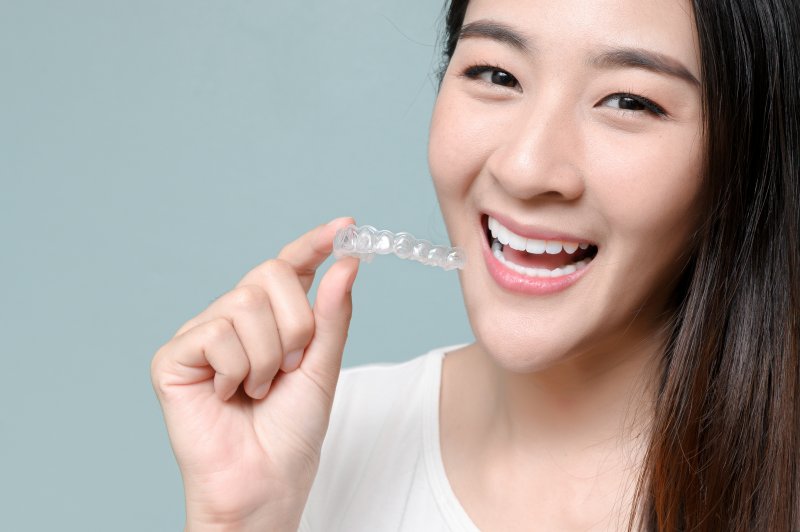 person smiling while holding clear aligners aligner